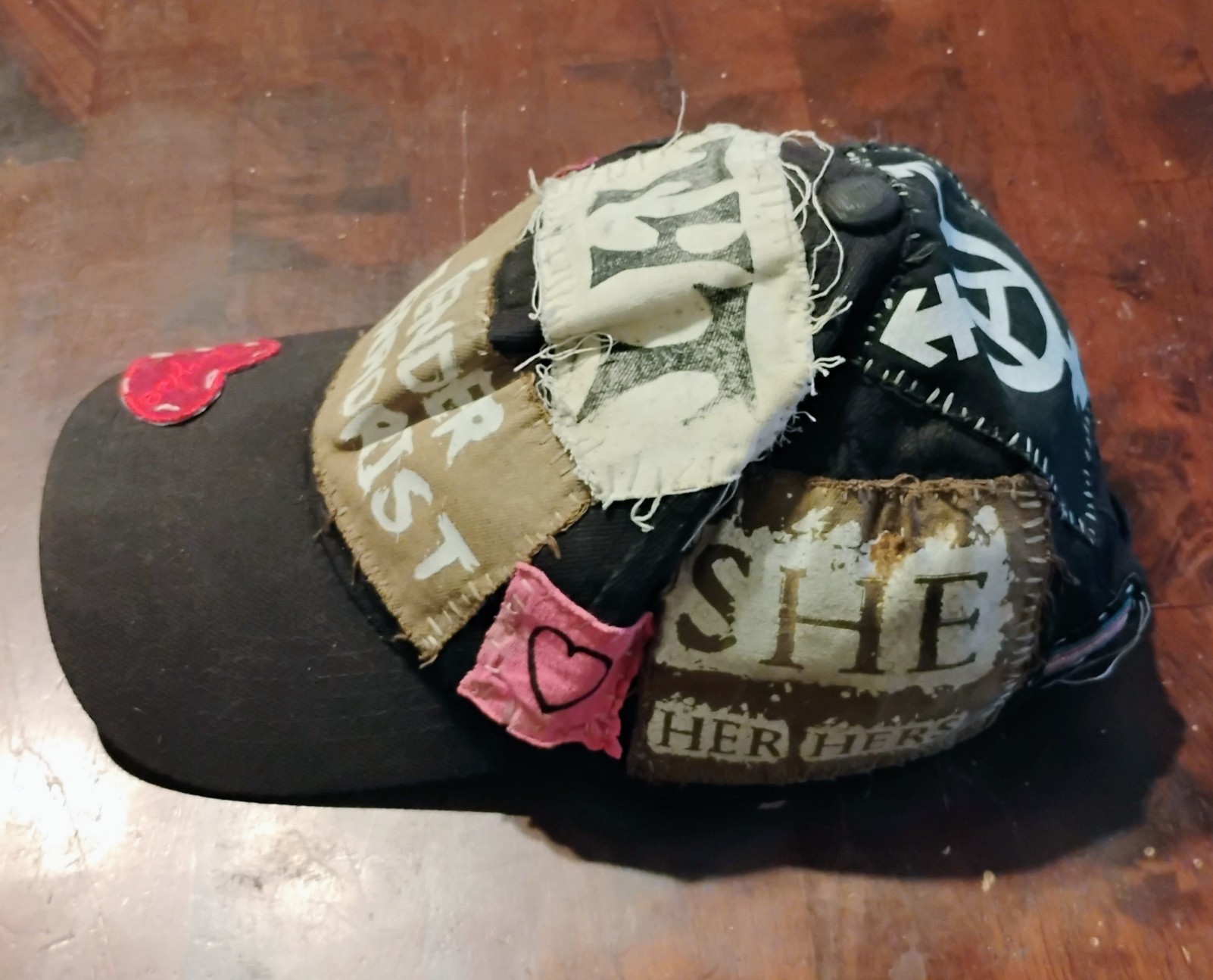 side of my gender terrorist hat with she/her pronoun and pink heart patches